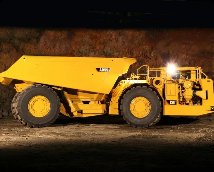 Большой желтый самосвал Caterpillar AD63 стоит на грунтовой дороге.