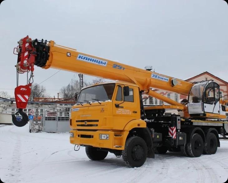 Жёлтый автомобильный кран на заснеженной территории.